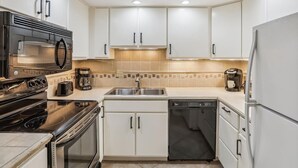 Una cocina moderna con armarios blancos, un microondas negro, una estufa, un lavavajillas y una cafetera.