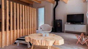 Ein gemütliches Zimmer mit einer Wand aus Holzlatten, einem runden Holztisch mit zwei Stühlen, einem Fernseher und einem Schrank.