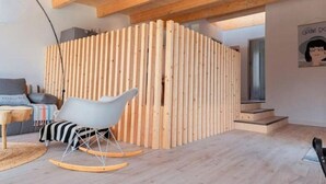 Ein modernes Interieur mit einer Holzwand, einem Schaukelstuhl und einer Treppe, die zu einer oberen Ebene führt.
