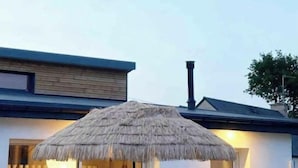 Ein modernes Haus mit einer Terrassenfläche, die einen Glastisch, Stühle, einen reetgedeckten Sonnenschirm und einen Blick ins Innere bietet.