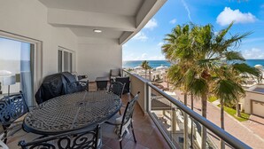 En balkon med et rundt bord og stole, der ud til et kystlandskab med palmer og en klar himmel.