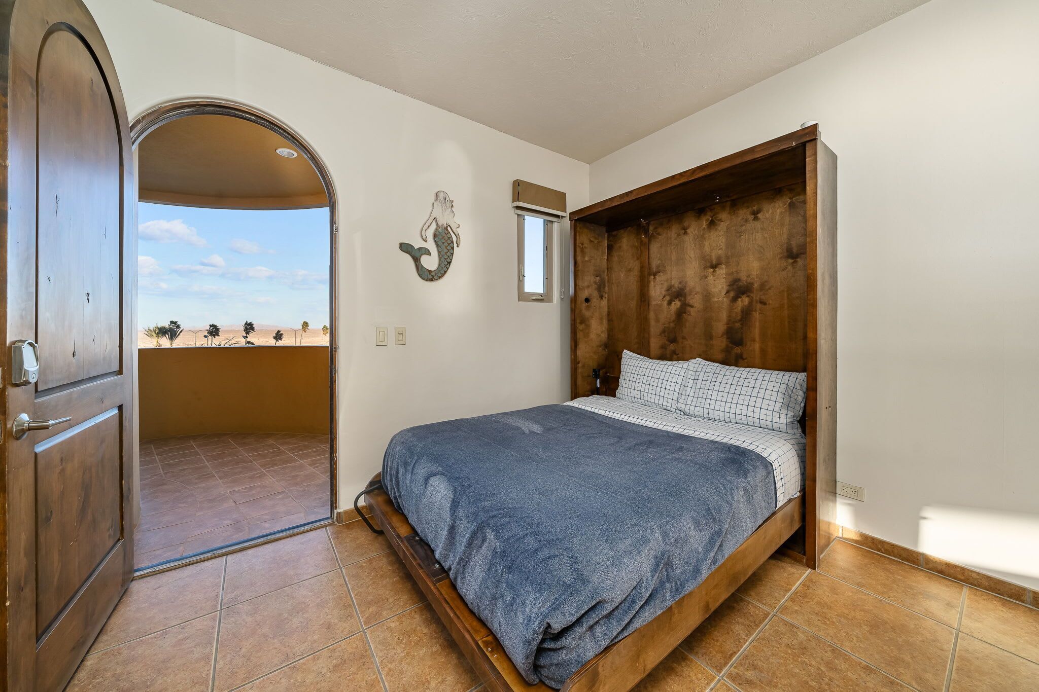 Una camera da letto con un letto in legno, vista attraverso una porta aperta e decorazione a tema sirena sul muro.