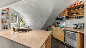 A kitchen with a stone arch, wooden shelves, a sink, and a refrigerator.