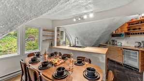 A modern kitchen with a wooden dining table set for six, a built-in oven, and a view of greenery outside.