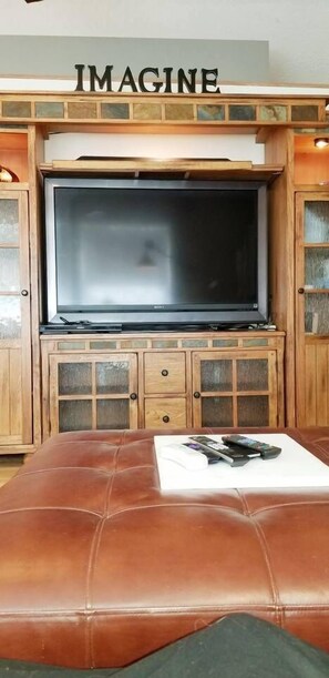 A living room with a large flat-screen TV mounted on a wooden cabinet with glass doors.