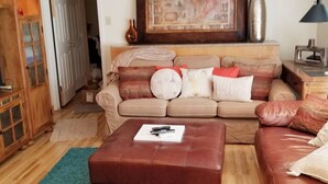 Ein Wohnzimmer mit einem beigen Sofa, einem braunen Lederhocker und einem Gemälde über dem Sofa.