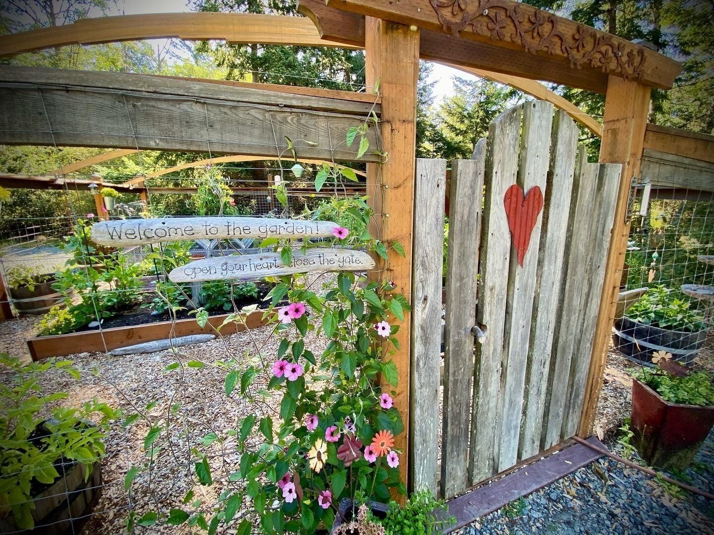 A wooden gate with a heart-shaped decoration, surrounded by a garden with various plants and flowers.