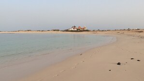 A sandy beach with footprints leading to a building with a white facade and a red roof. - El Cotillo Sonando,Couples only, Romantic,Minutes from swim/surf,Well equipped. (El Cotillo)
