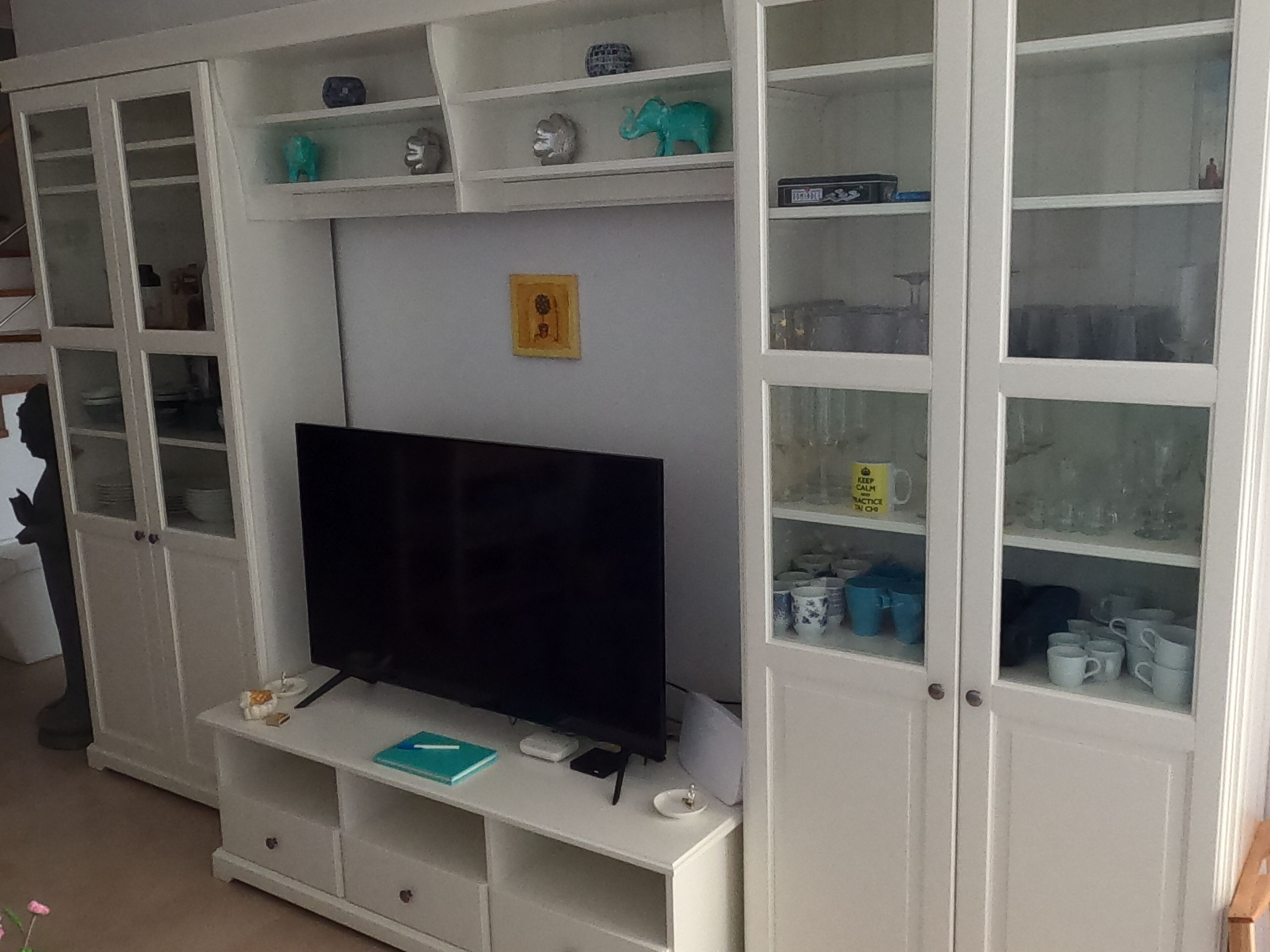 Un salón con televisor de pantalla plana, armarios blancos y estanterías con adornos.
