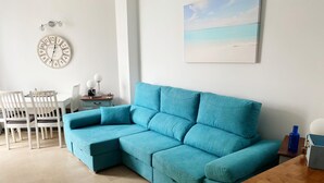 A modern living room with a teal sofa, a wooden coffee table, and a painting of a beach. - El Cotillo Sonando,Couples only, Romantic,Minutes from swim/surf,Well equipped. (El Cotillo)