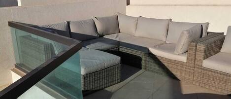 Eine Dachterrasse mit Glasbrüstung, einer Sofagruppe und einem Liegestuhl.
