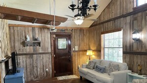 Un intérieur rustique avec des murs en bois, un canapé blanc, un pouf à motifs et un ventilateur de plafond.