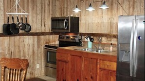Une cuisine avec des meubles en bois, un réfrigérateur en acier inoxydable, un four à micro-ondes et des casseroles suspendues.