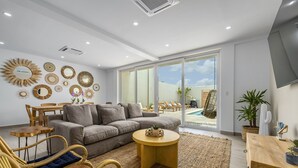 Un salon moderne avec un canapé gris, des fauteuils en osier, une table basse ronde et un coin repas comprenant une table et des chaises en bois.