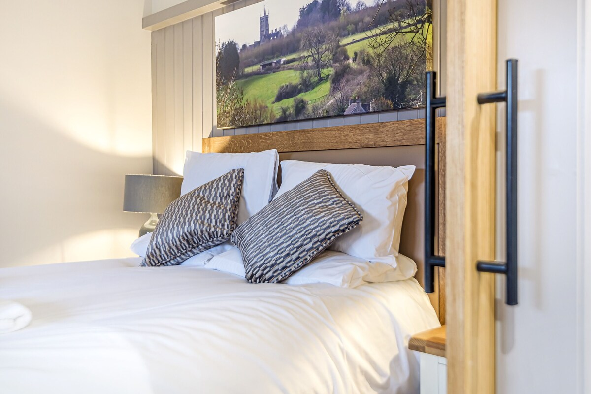 Una cama bien hecha con almohadones estampados, un cabecero de madera y un cuadro grande de un paisaje sobre ella.