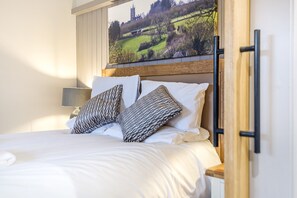 A neatly made bed with patterned pillows, a wooden headboard, and a large landscape painting above it.