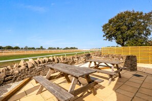 Un espace pique-nique avec des bancs en bois et un muret en pierre, donnant sur un champ verdoyant.