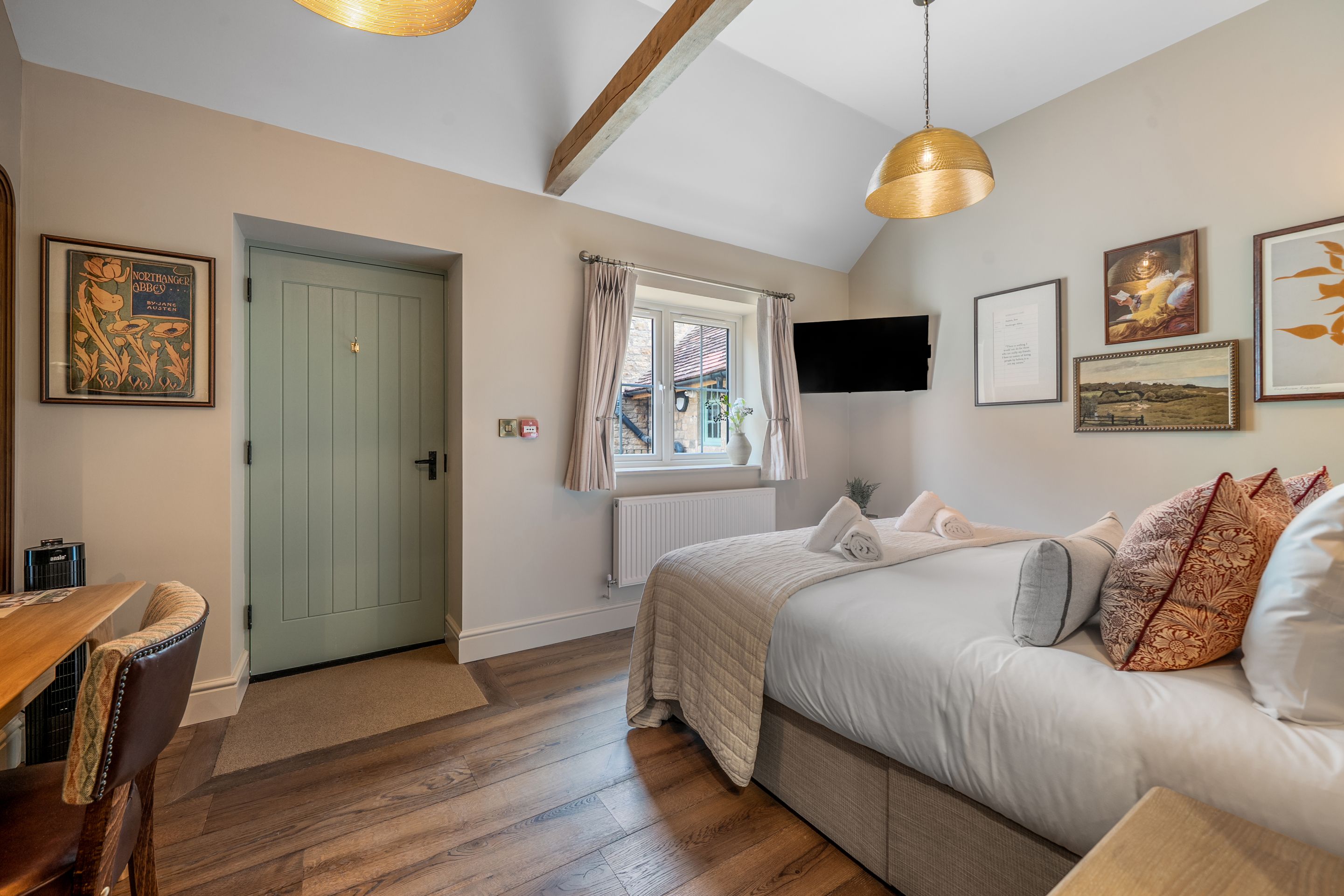Un dormitorio con cama, escritorio, silla, ventana con cortinas y obra de arte en la pared.