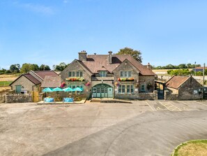 Un bâtiment en pierre avec une porte verte, de nombreuses fenêtres et des jardinières. On peut voir des parapluies et une enseigne indiquant « The Charcombe Inn ».