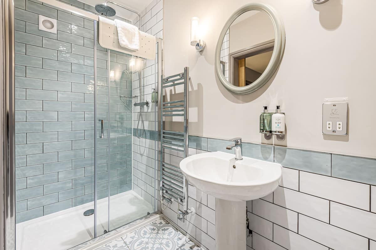 Un baño con cabina de ducha de vidrio, un lavabo blanco, un espejo redondo y un perchero para toallas.