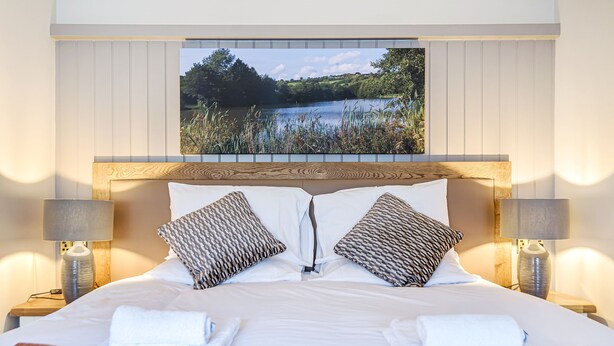 A hotel room with a wooden headboard, two patterned pillows, a bed with white linens, and a view of a lake through a window. - Charlcombe Inn (Bath)