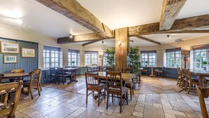 A spacious dining area with wooden tables and chairs, large windows, and exposed wooden beams on the ceiling. - Charlcombe Inn (Bath)
