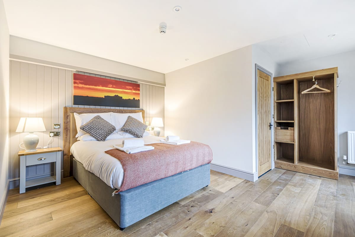 Un dormitorio con una cama, mesitas de noche, un cuadro, un armario de madera y suelo de madera.