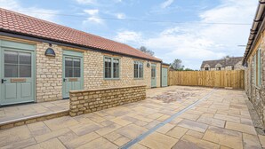 A stone building with green doors and windows, a tiled patio, and a wooden fence. - Charlcombe Inn (Bath)