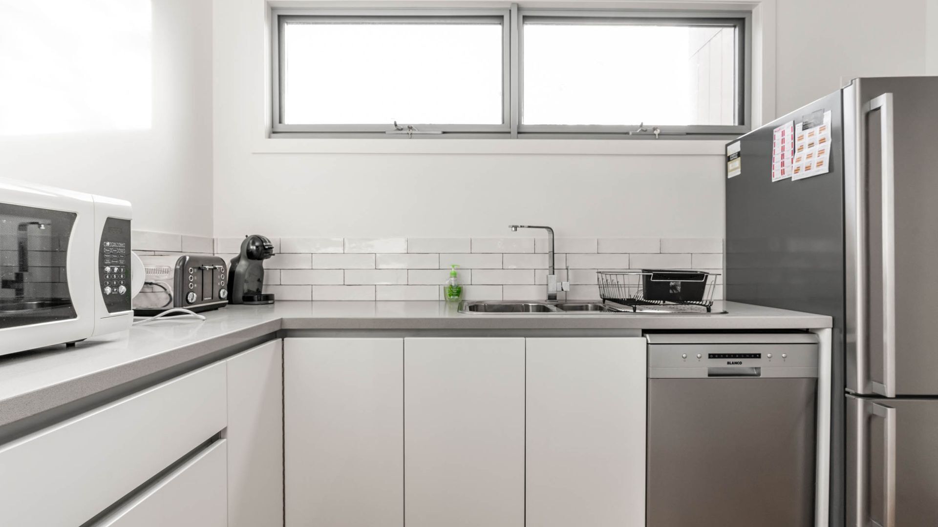 Een moderne keuken met witte kastjes, een roestvrijstalen koelkast, een magnetron, een broodrooster en een spoelbak.