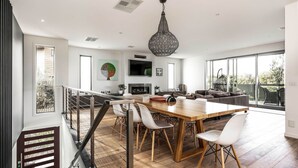 Amplia sala de estar con mesa de comedor de madera, sillas blancas, chimenea y un ventanal con vistas al exterior.