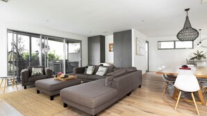 Una sala de estar moderna con un sofá modular, una mesa de comedor y un amplio ventanal corredera que da a un balcón.