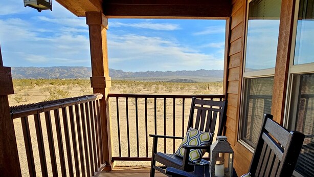 A wooden deck with two rocking chairs and a lantern, overlooking a desert landscape. - Spectacular panoramic views on nearly 10 acres, Stargazing, Spa, Family Friendly (Twentynine Palms)