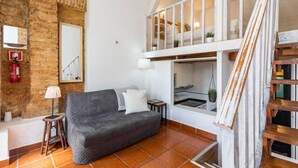 Uma sala de estar moderna com um sofá cinzento, uma mesinha lateral, uma luminária e um extintor de incêndio na parede.