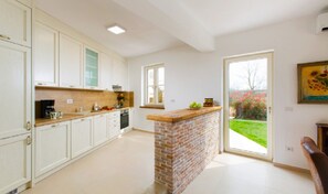 Een keuken met witte kasten, een keukeneiland van baksteen en een schuifdeur naar een tuin.