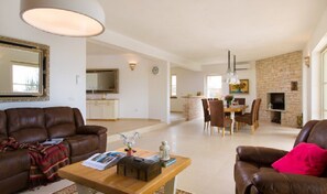 Een ruime woonkamer met een bruine leren bank, een houten salontafel en een eethoek met een bakstenen muur en een open haard.