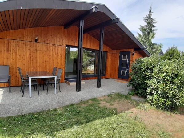 A modern wooden building with a covered patio area, a dining table with chairs, and a door with glass panels. - Vacation home for up to 6 people in the beautiful Black Forest (Schramberg)