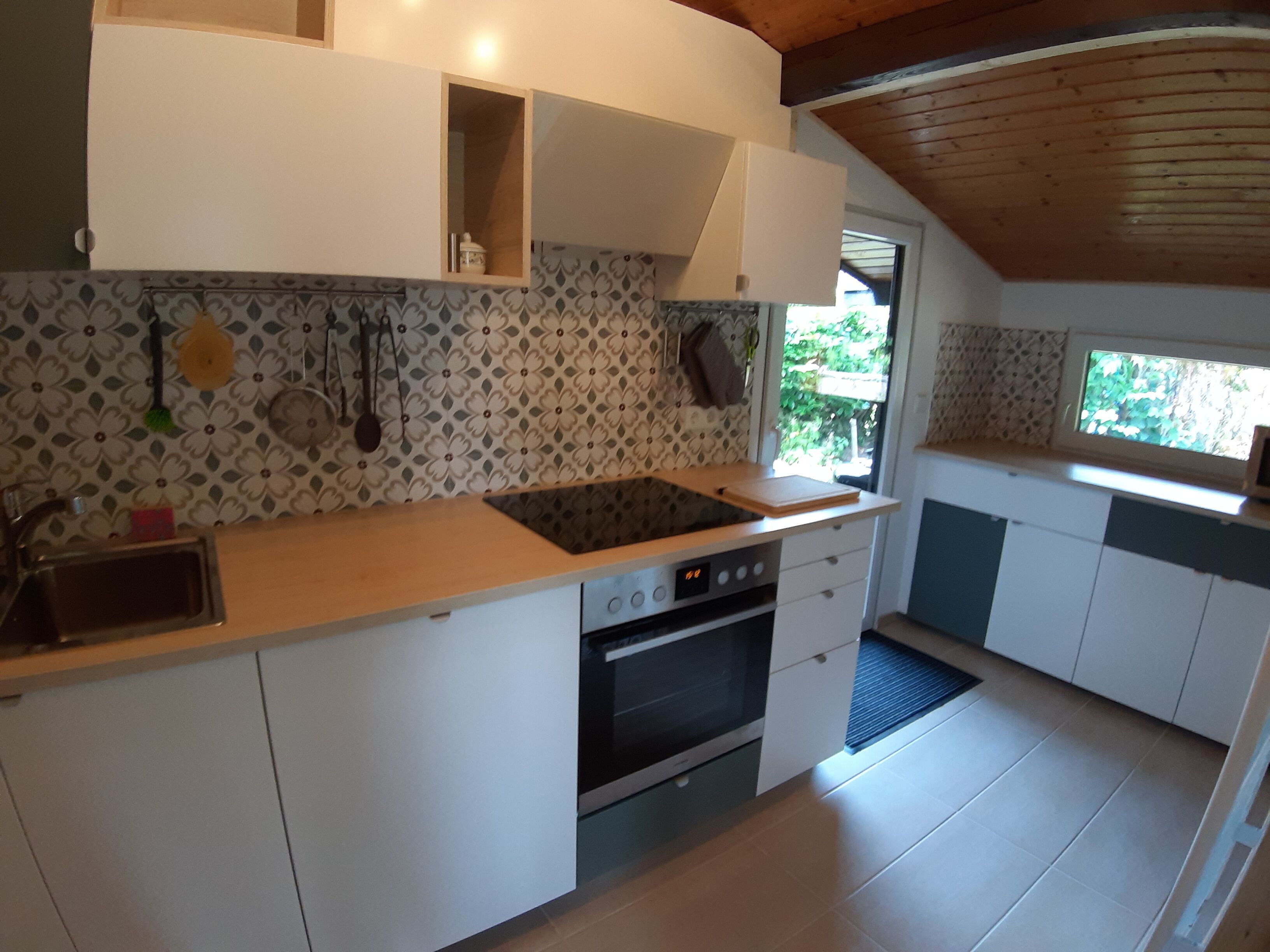 Une cuisine moderne avec des meubles blancs, une cuisinière noire et une fenêtre qui laisse entrer la lumière naturelle.