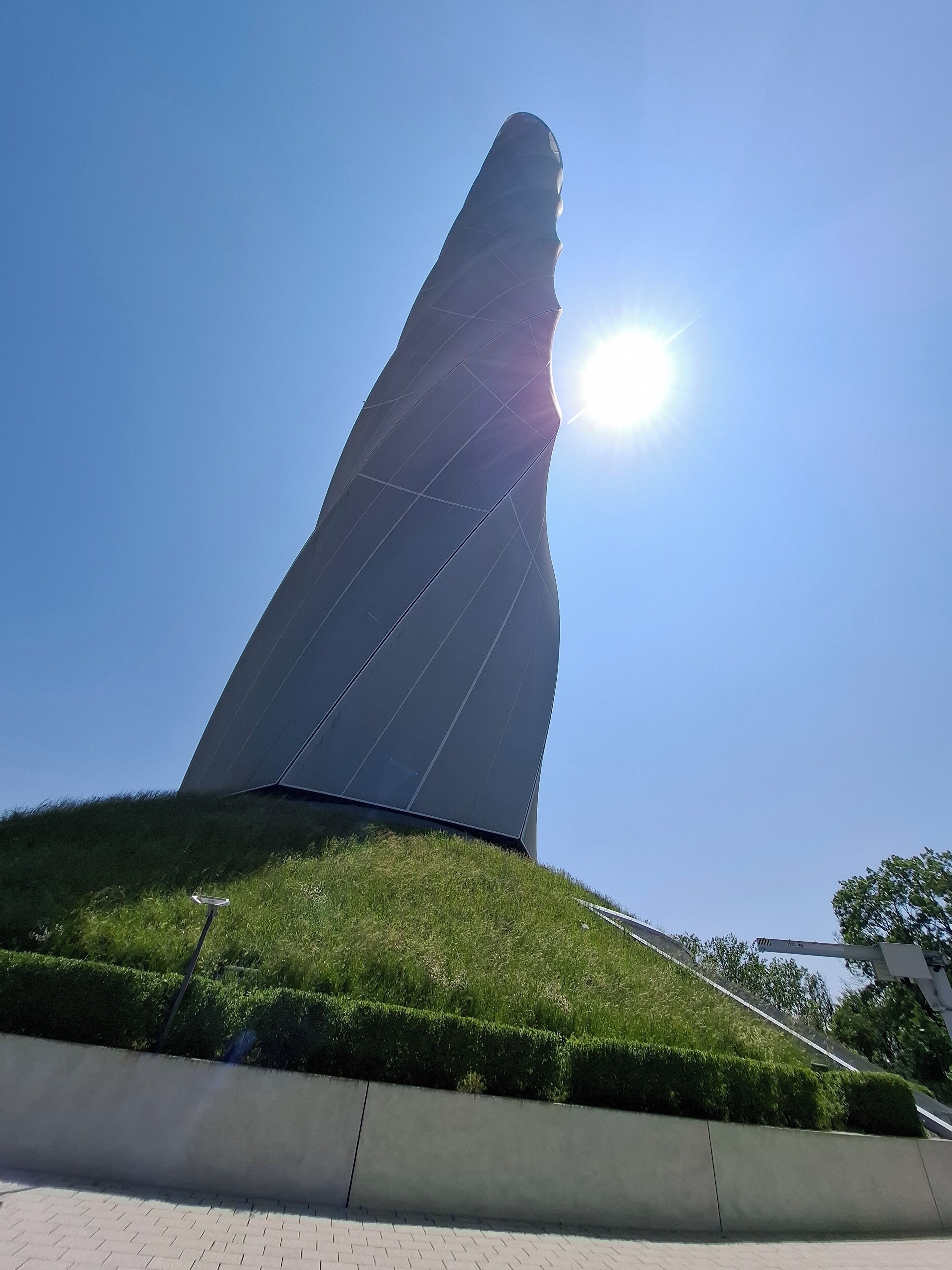 A modern building with a unique, curved roof design, situated on a grassy hill with a clear blue sky in the background.