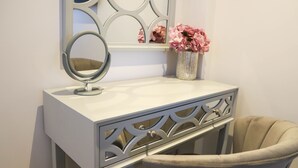 A white vanity with a mirror, a vase with pink flowers, and a chair. - Apartment Seven (Shrewsbury)
