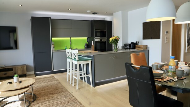 A modern kitchen with a central island, bar stools, a dining table, and a large pendant light. - Apartment Seven (Shrewsbury)
