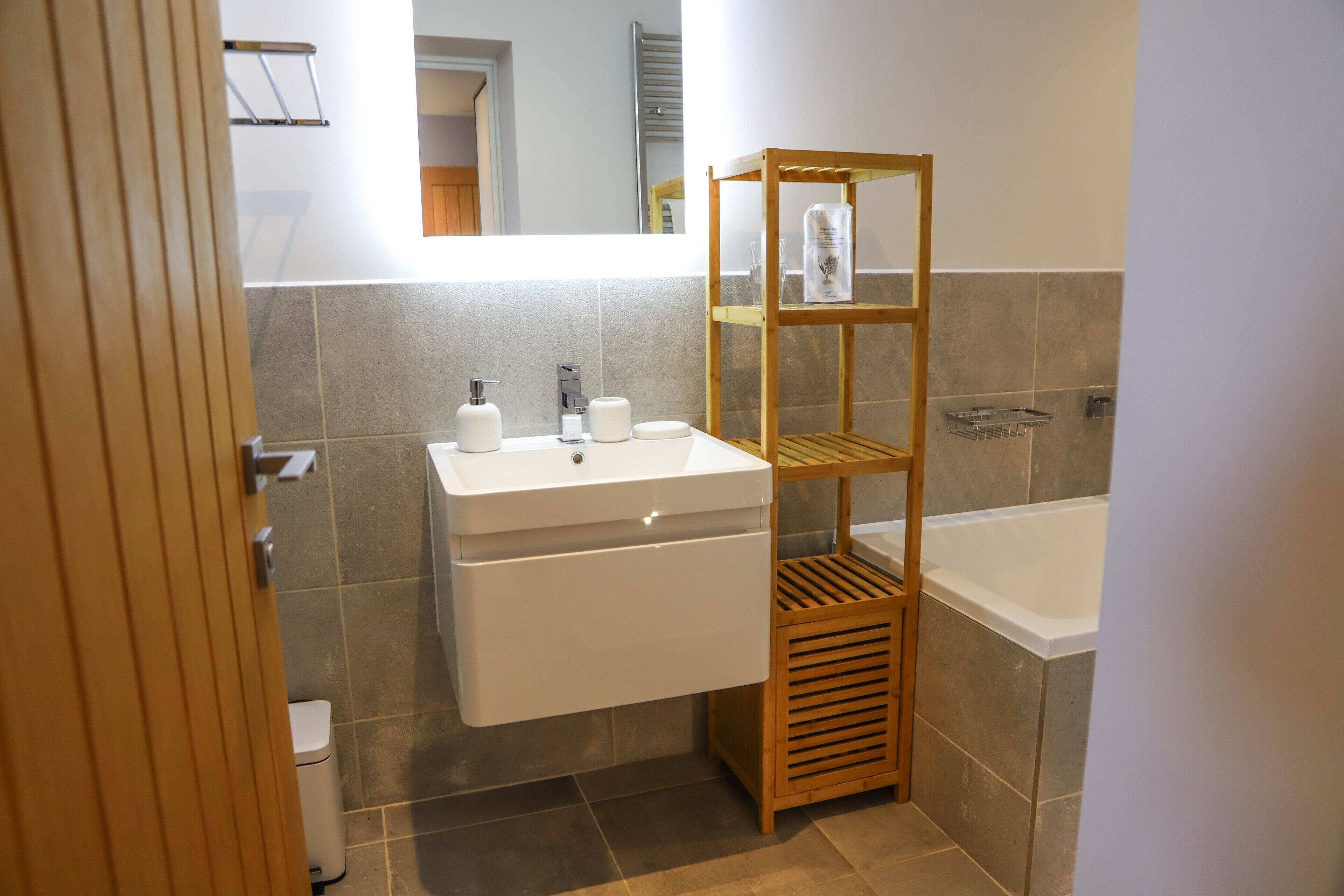 A bathroom with a wooden shelf holding toiletries, a white sink, and a bathtub.