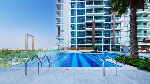 A modern hotel with a large swimming pool, a palm tree, and a high-rise building in the background. - Maison Privee - Superb 1BR apartment overlooking Zabeel Park and Dubai Frame (Dubai)