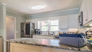 Una cocina con armarios azul claro, encimera de mármol, refrigerador, cafetera y una bolsa a rayas sobre la encimera.