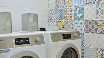Un espace buanderie comprenant deux machines à laver et un panneau de commande, le tout installé devant un mur recouvert de carreaux décoratifs.
