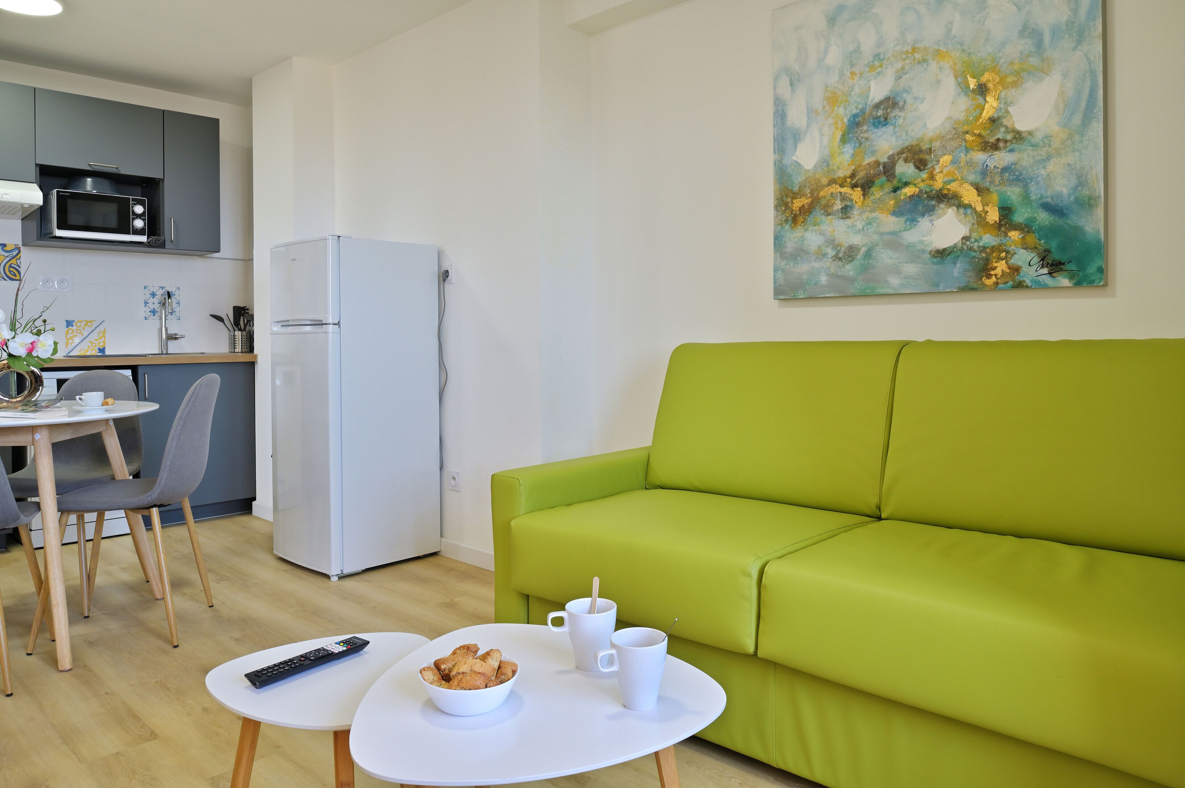 Un salon moderne avec un canapé vert, une table à manger avec des chaises, un réfrigérateur blanc et un four à micro-ondes placé au-dessus du plan de travail.