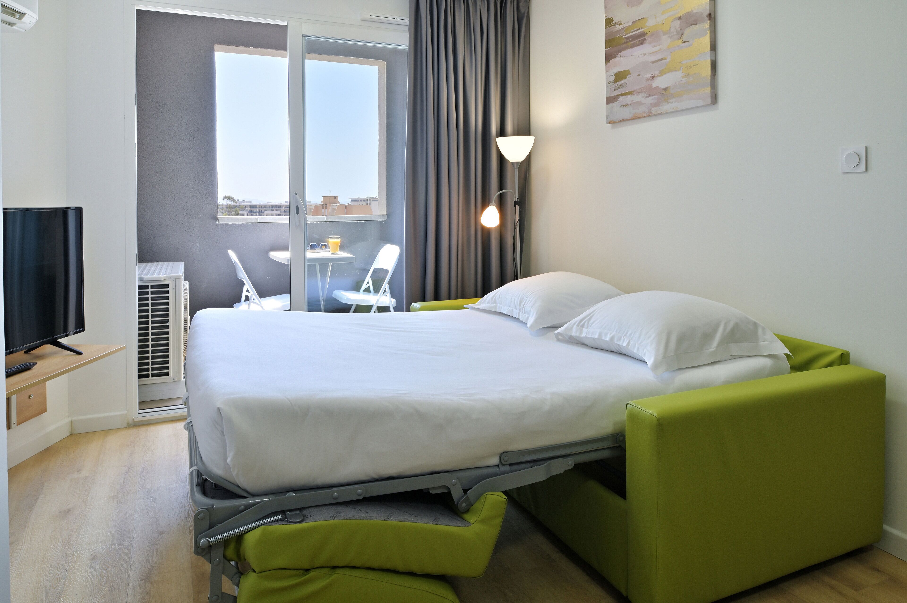 A modern hotel room with a bed, a desk, a chair, and a TV.
