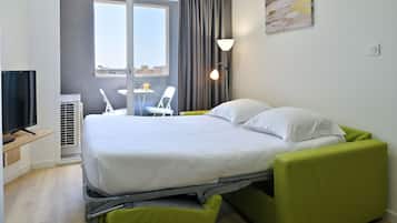 A modern hotel room with a bed, a desk, a chair, and a TV.