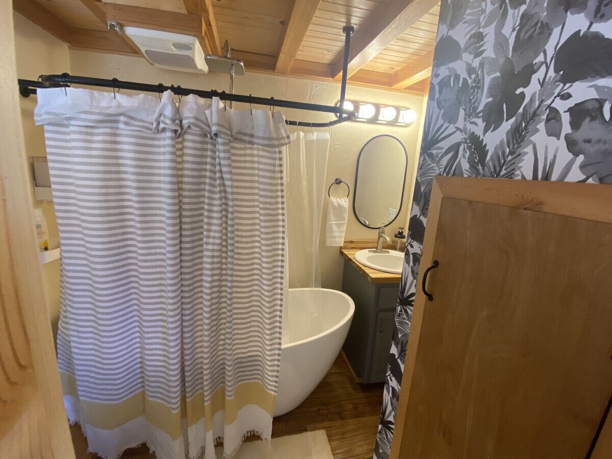Ein Badezimmer mit einer großen weißen Badewanne, einem hölzernen Waschtisch und einem gestreiften Duschvorhang.