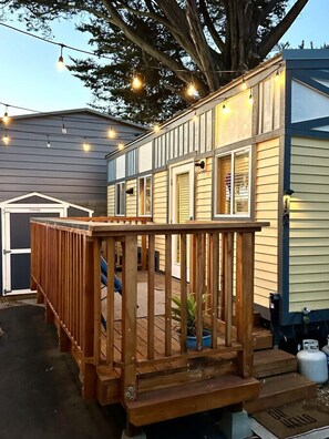 A wooden deck with a railing, a small potted plant, and a propane tank. - San Luis Obispo Sunshine Tiny Home with 2 Queens (San Luis Obispo)