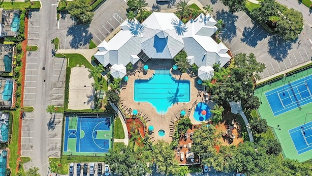 Vista aérea de un complejo turístico con piscina central, canchas de tenis y zona de estacionamiento.